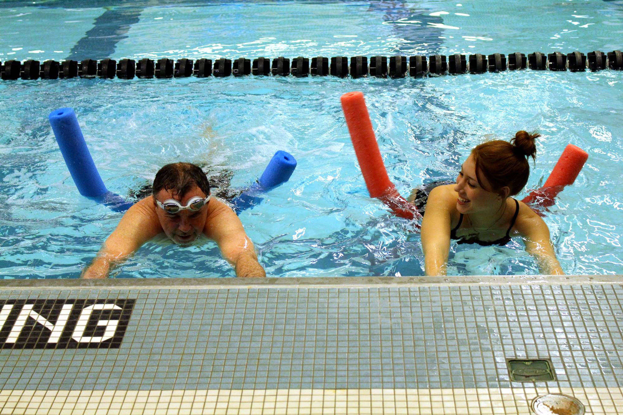Participant and Swim instructor in the pool on noodles practicing kicks.